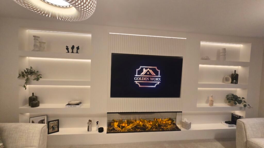 White built-in entertainment wall with backlit shelves, a central TV showing the 'GOLDEN WORX' logo, and a fireplace below.